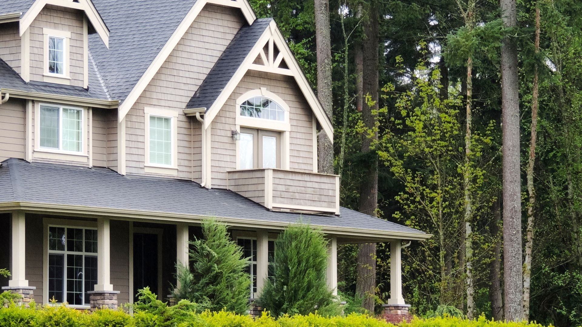 Large two-story house with gabled roof surrounded by lush green forest